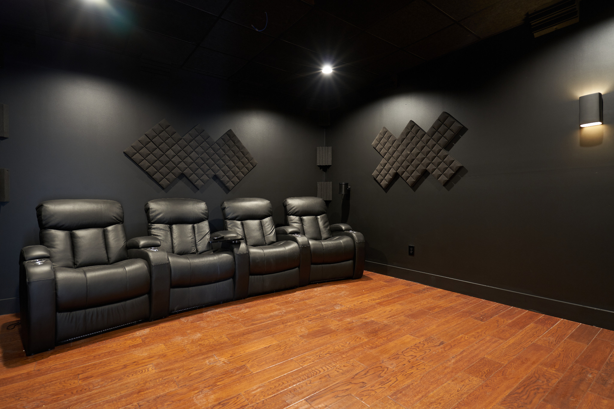 Home theater with four black leather recliners, dark walls, acoustic panels, and recessed lighting