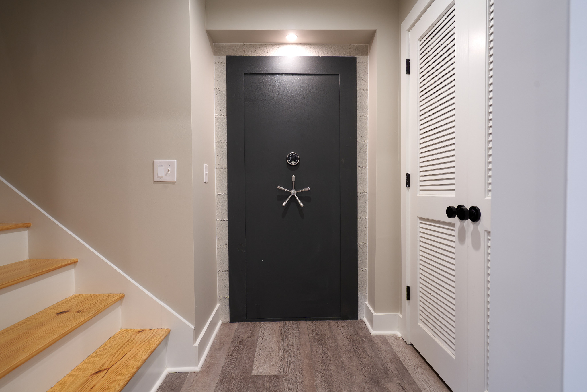Black steel vault door with a combination lock and wheel handle beside the basement staircase