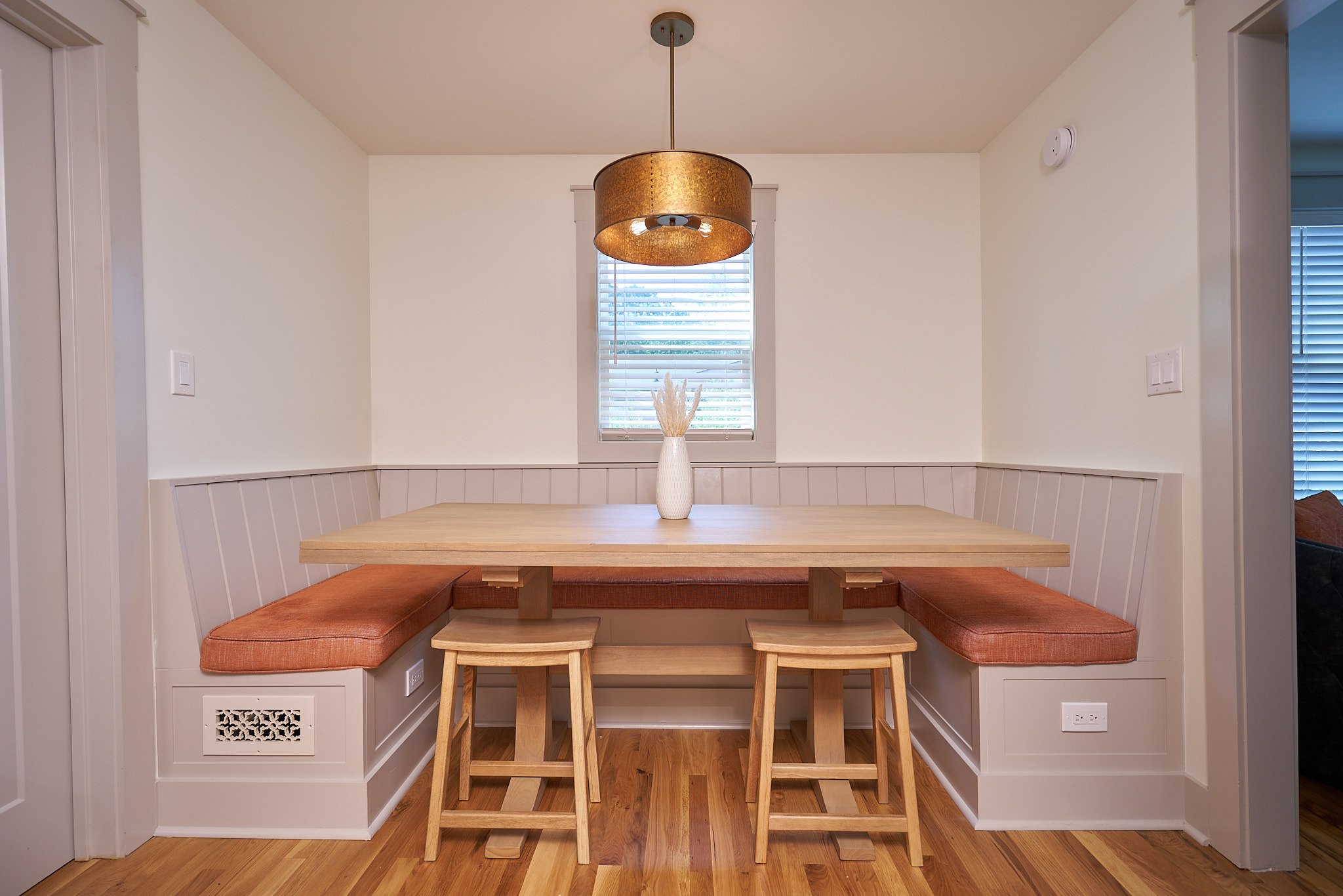 Custom U-shaped dining banquette with upholstered seating, a wood table, and refinished hardwood flooring