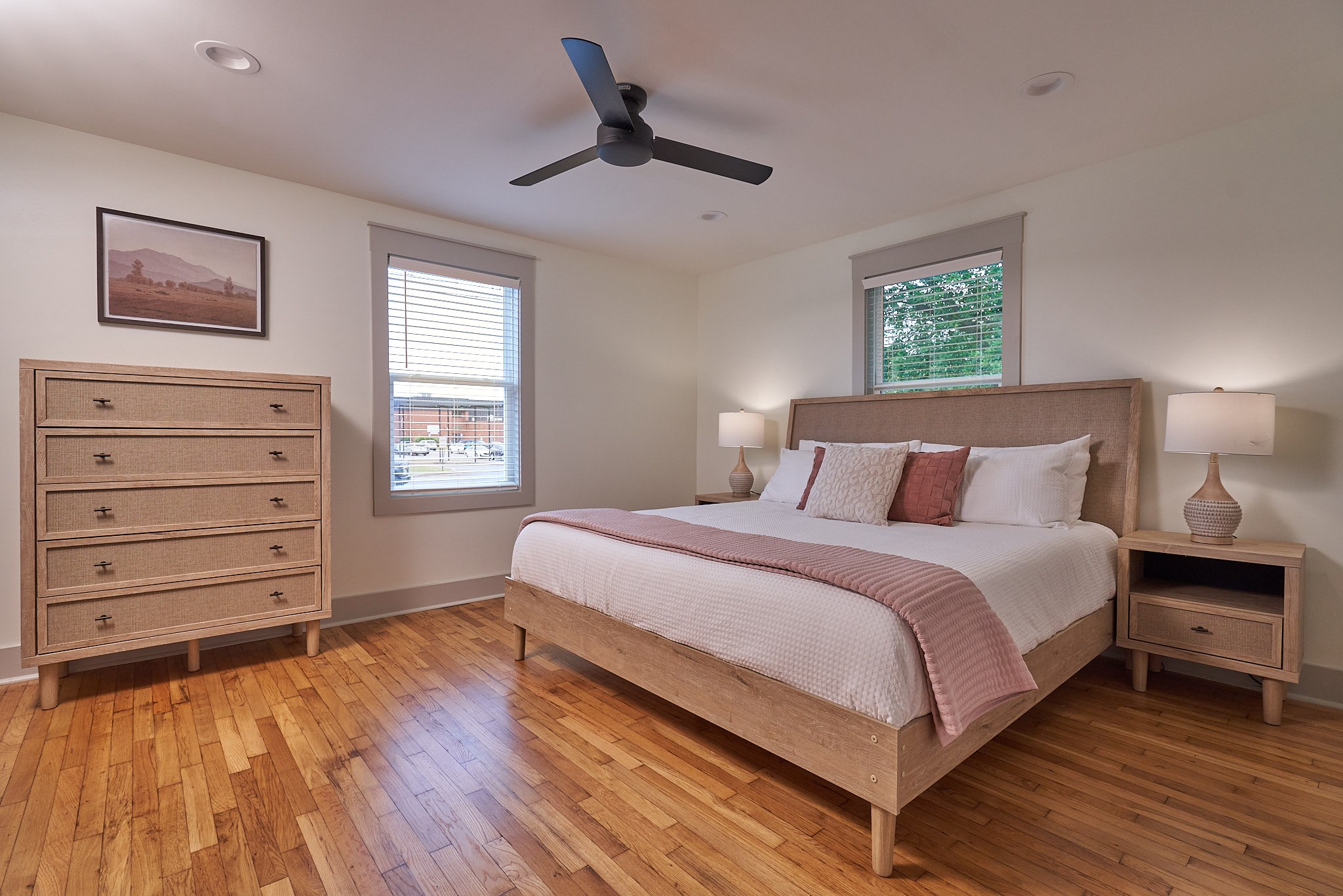 Finished guest bedroom with wood furniture, neutral bedding, a ceiling fan, and refinished hardwood floors