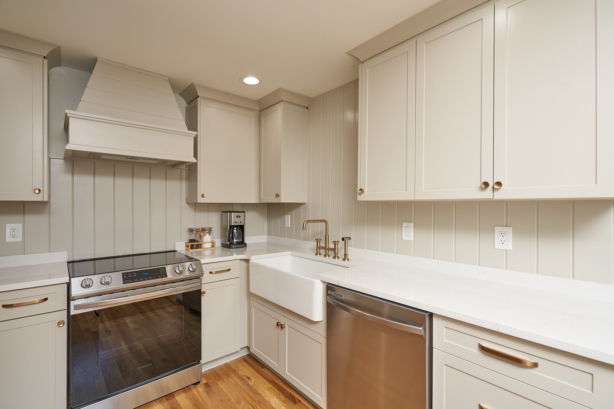 Renovated kitchen with warm gray cabinets, white countertops, a farmhouse sink, and brass fixtures
